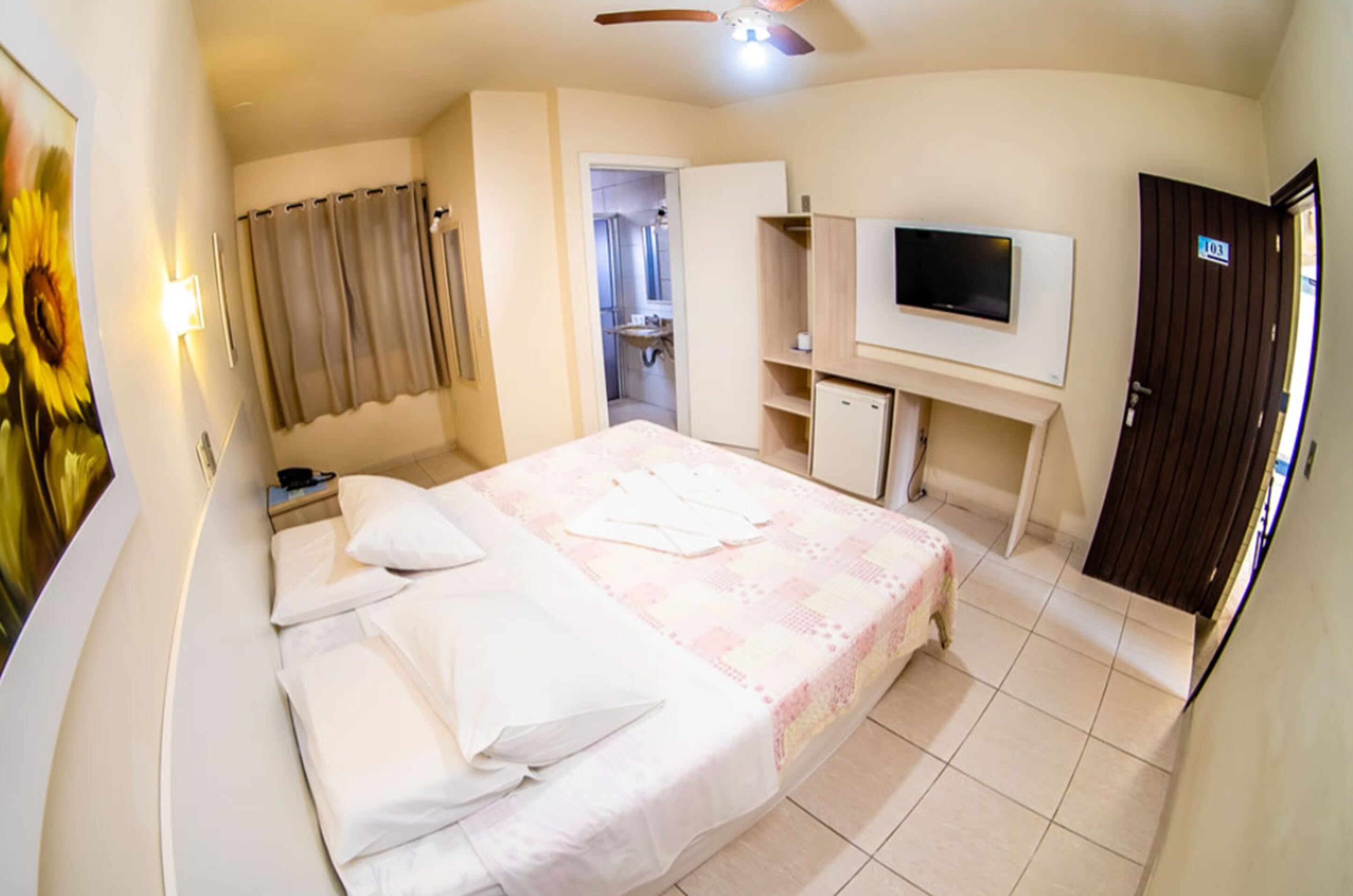 Un dormitorio con cama, televisor, armario y baño visible a través de una puerta abierta.