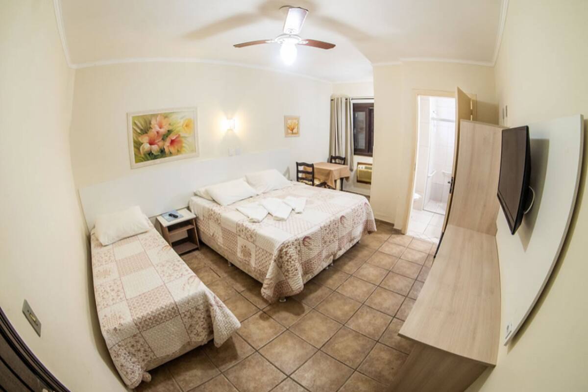 A hotel room with two beds, a desk, a chair, a TV, and a ceiling fan.