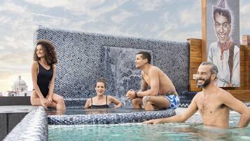 Una piscina en la azotea con mosaicos, vistas a la ciudad y un gran retrato en la pared.