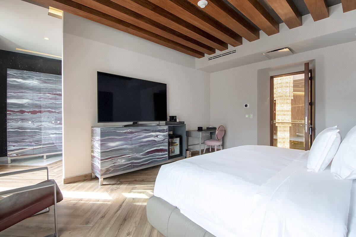 A modern bedroom with a large bed, a flat-screen TV mounted on a marble cabinet, and a large window with a view.
