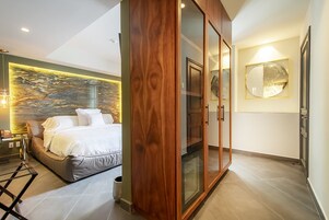 Een moderne slaapkamer met een bed, een houten garderobe, een wandlamp en een decoratief wandpaneel.