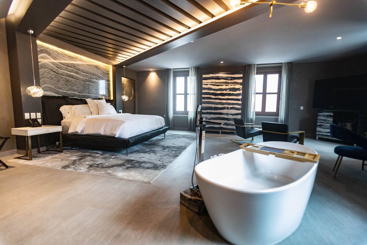 A modern bedroom with a large bed, a bathtub, and a desk.