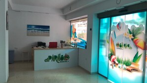 Un comptoir d’accueil orné d’un logo, une fenêtre offrant une vue agréable et une porte décorée d’une fresque aux motifs tropicaux.