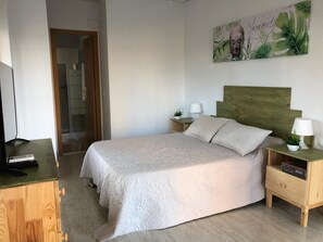 A bedroom with a bed, wooden headboard, bedside tables with lamps, a painting on the wall, and a television on a wooden dresser. - Hostal El Paraíso (Alicante)