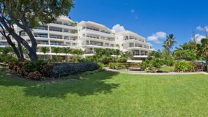 A hotel with a large lawn, palm trees, and a pool area. - Palm Beach Condo 202  - A Vacation Rental by Bougainvillea Barbados (Hastings)