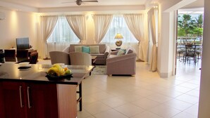 A spacious living room with a sofa set, a dining area with a table and chairs, and a balcony with a view of the outdoors. - Palm Beach Condo 202  - A Vacation Rental by Bougainvillea Barbados (Hastings)