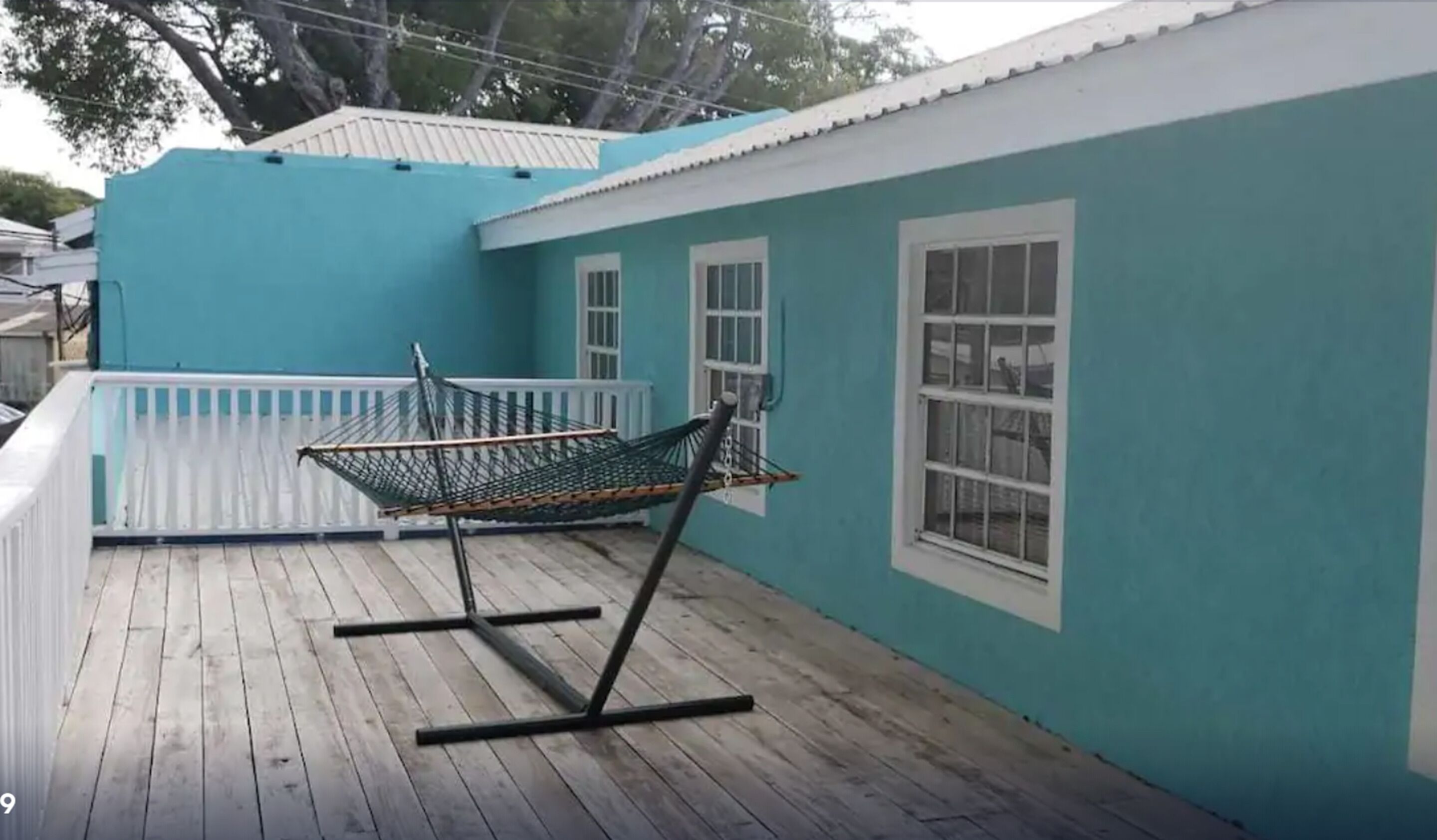 Une maison bleue avec une terrasse en bois, un hamac et une balustrade blanche.