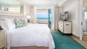 A bedroom with a large bed, a television, a dresser, and a view of the ocean.