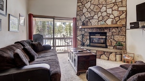 A living room with a stone fireplace, a sofa, a coffee table, and a TV mounted on the wall. - 3bd_atrium_302 (Breckenridge)
