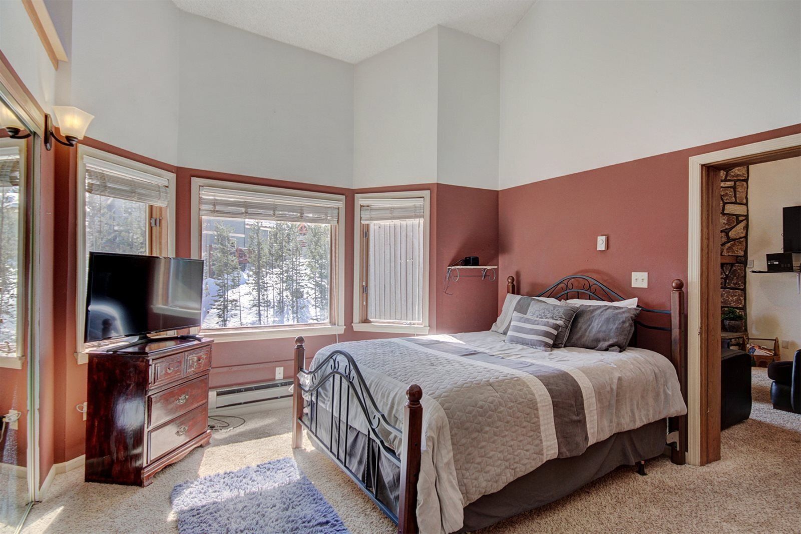 A bedroom with a bed, dresser, TV, and windows.