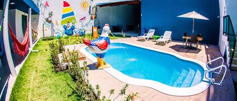 Una piscina con un mural colorido, asientos exteriores y un cielo despejado.