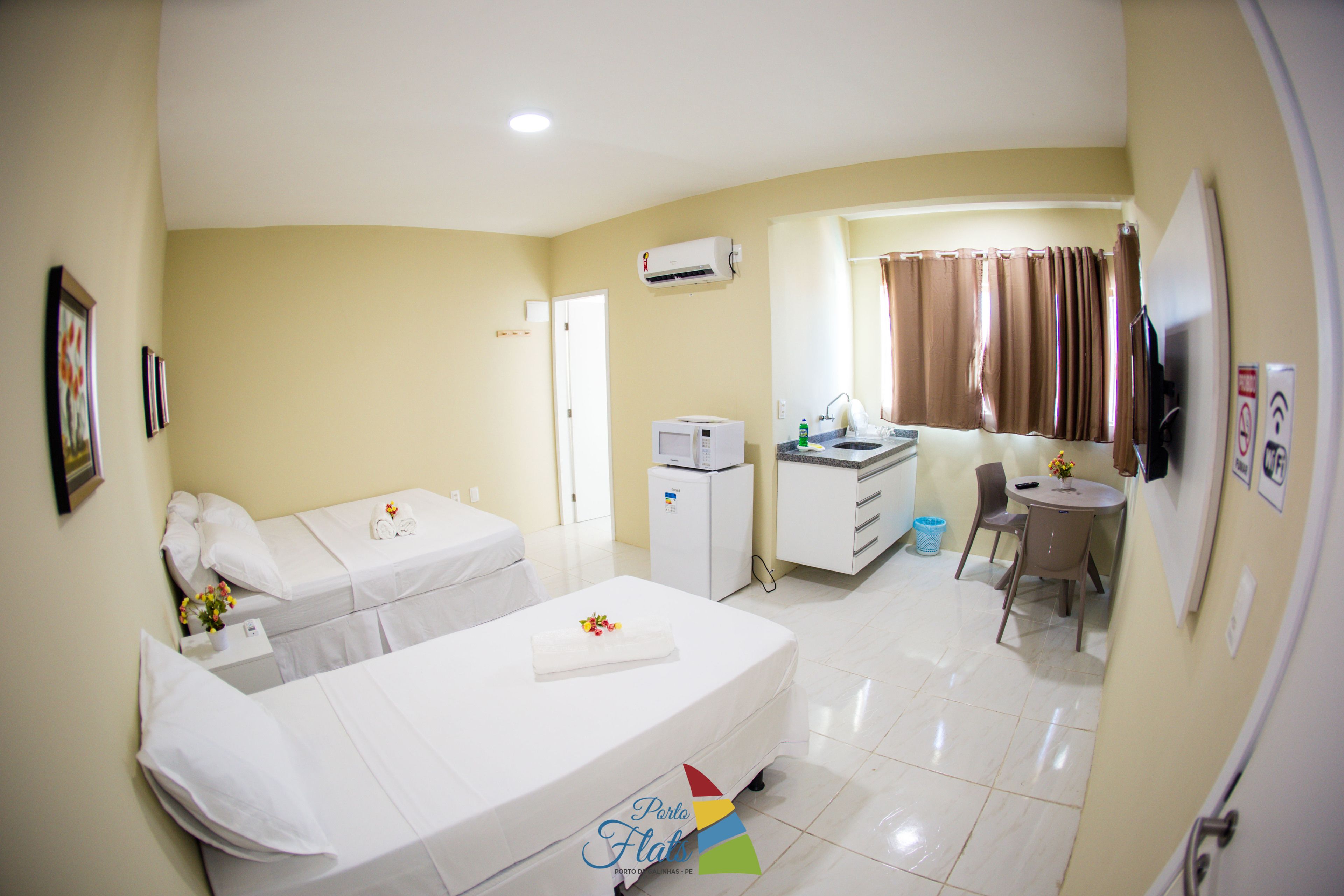 Habitación de hotel con dos camas, un kitchenette pequeño, un baño y una zona de comedor.
