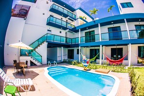 A modern building with a swimming pool, outdoor seating, and a hammock.