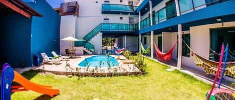A pool area with a slide, lounge chairs, and a hammock.