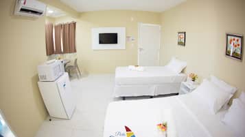 A hotel room with two beds, a desk, a chair, an air conditioning unit, a television, and a door.