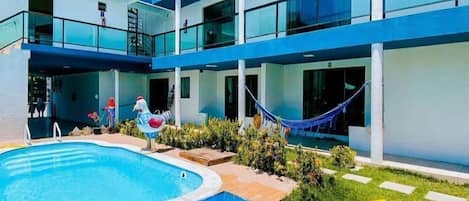 Un edificio moderno con piscina, varios balcones y un área verde con hamaca.