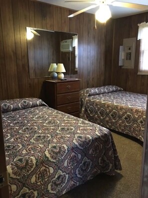 A room with two beds, a dresser, a mirror, and a ceiling fan.