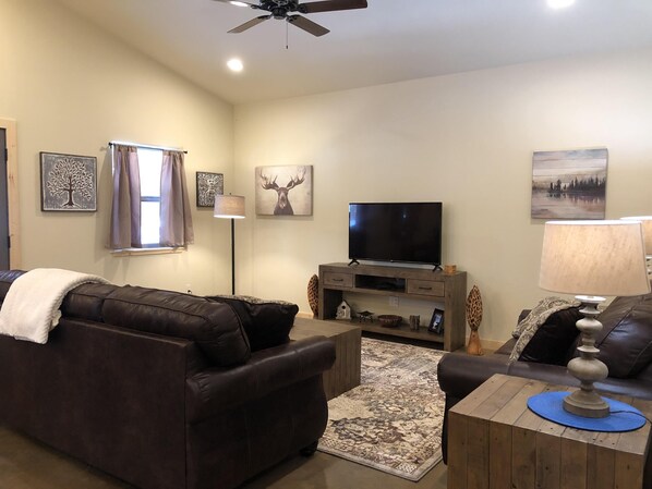 A living room with a brown leather sofa, a wooden coffee table, a television on a wooden stand, and a floor lamp.