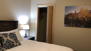 A bedroom with a bed, a bedside lamp, a wooden door, and a landscape painting on the wall.