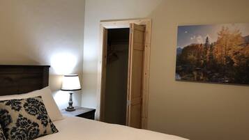 A bedroom with a bed, a bedside lamp, a wooden door, and a landscape painting on the wall.