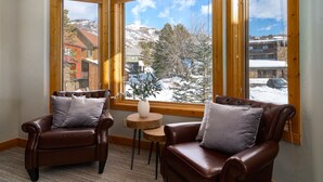 Una habitación con dos sillones de cuero, una mesita de madera y una ventana que ofrece vistas a una montaña nevada y edificios.