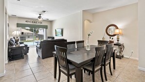 Un coin repas avec une table et des chaises en bois foncé, un vase de fleurs et une lampe sur une petite table d’appoint.