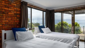 A hotel room with two beds, a brick wall, large windows, and a balcony with a view. - Jewel of Gerroa, Gerroa, South Coast (Gerroa)