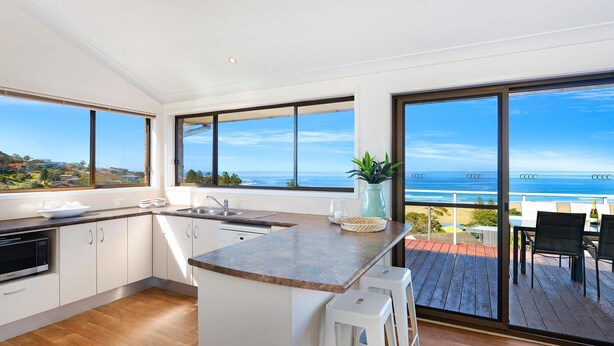 A modern kitchen with large windows, a view of the ocean, and a deck with outdoor seating. - Jewel of Gerroa, Gerroa, South Coast (Gerroa)