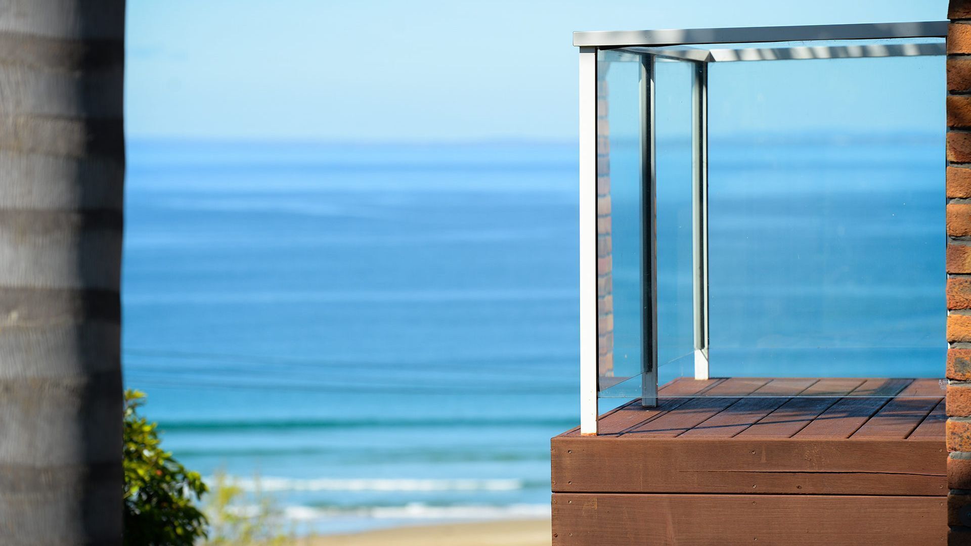 A balcony with a glass enclosure overlooking a beach.
