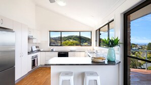 A modern kitchen with a large window, wooden flooring, and a view of a hilly landscape. - Jewel of Gerroa, Gerroa, South Coast (Gerroa)