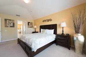 A bedroom with a large bed, two bedside tables with lamps, a decorative wall piece, and a tall vase with branches.