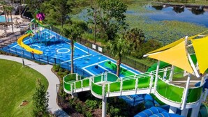 Ein Wasserpark mit einem blauen Spielbereich, grünen Rutschen und einem gelben Sonnensegel.