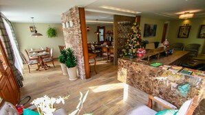A spacious living area with a wooden floor, a brick accent wall, and a Christmas tree. There is a dining area with a table and chairs, and a seating area with a sofa and a coffee table. - Pousada Caminho dos Plátanos (Gramado)