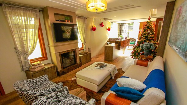 A living room with a fireplace, a sofa, a patterned armchair, and a Christmas tree. - Pousada Caminho dos Plátanos (Gramado)