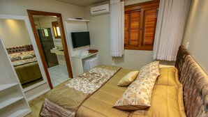 A bedroom with a bed, a TV, a desk, and a bathroom visible through an open door. - Pousada Caminho dos Plátanos (Gramado)