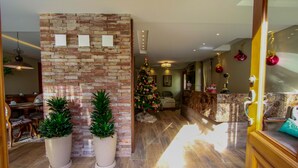 A spacious living area with a brick wall, potted plants, a Christmas tree, and a wooden reception desk. - Pousada Caminho dos Plátanos (Gramado)