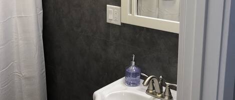 A bathroom with a white sink, a mirror, a shower curtain, and a dark tiled wall.