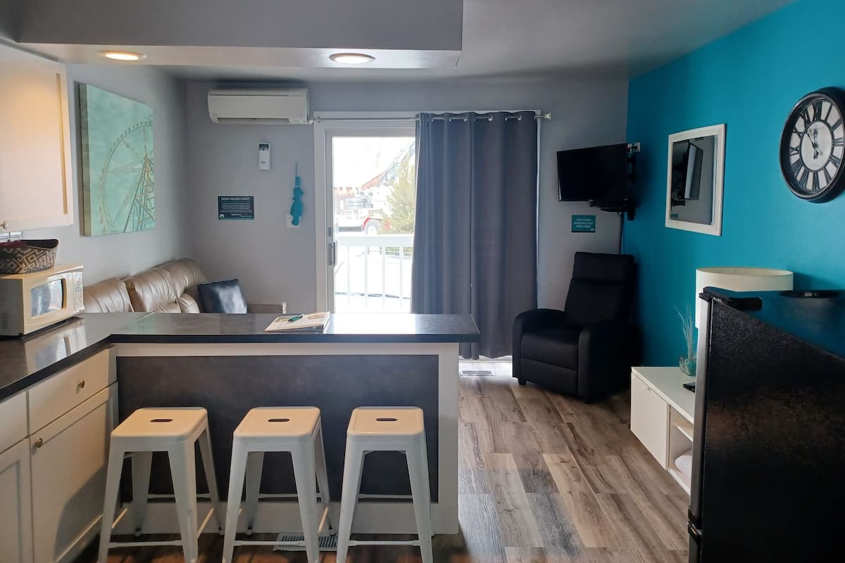 Eine moderne Küche mit einer zentralen Kochinsel, Barhocker, einer Sitzecke mit einer Couch und einem an der Wand befestigten Fernseher.