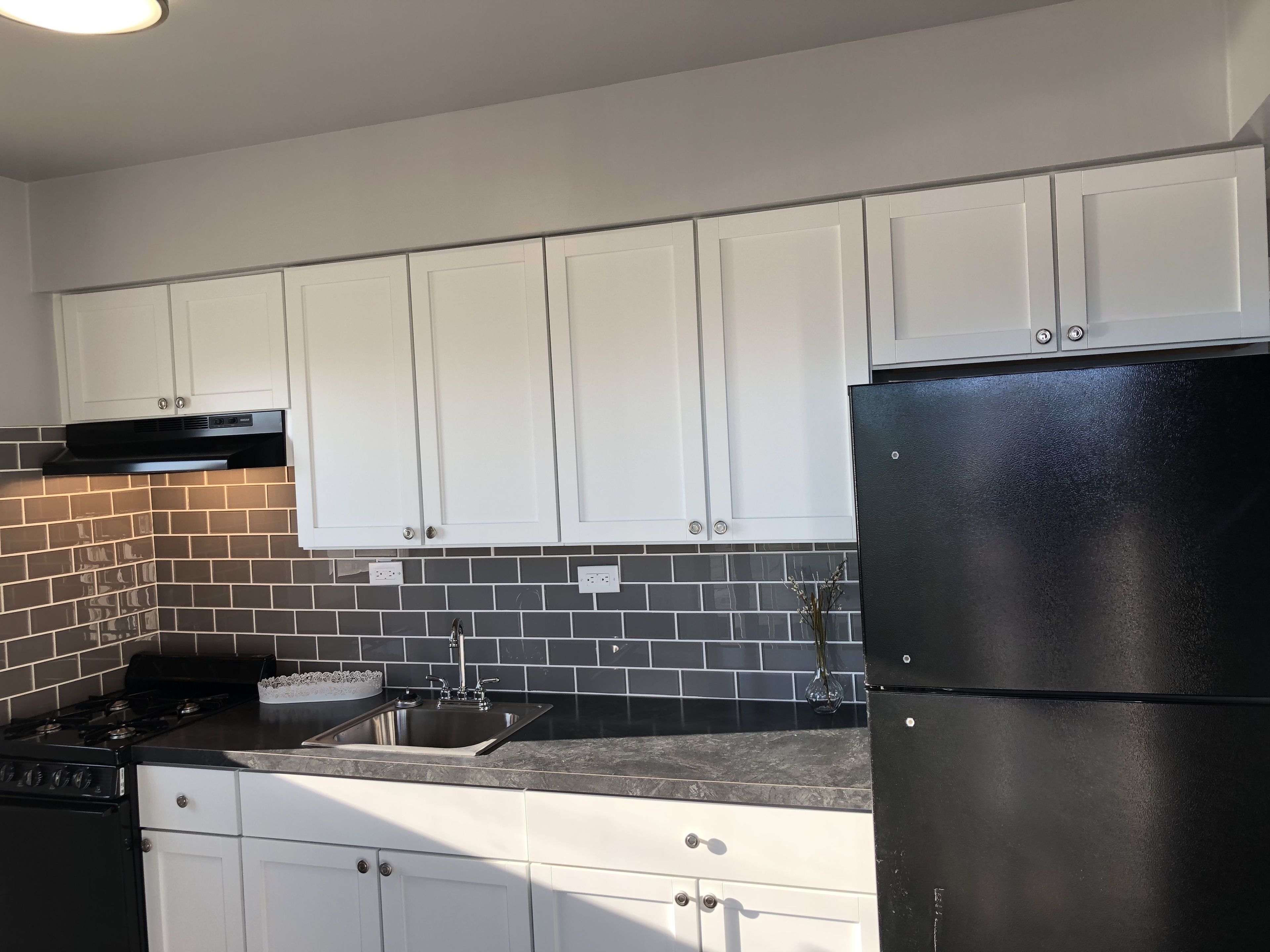 Cozinha moderna com armários brancos, geladeira preta e painel de azulejos.