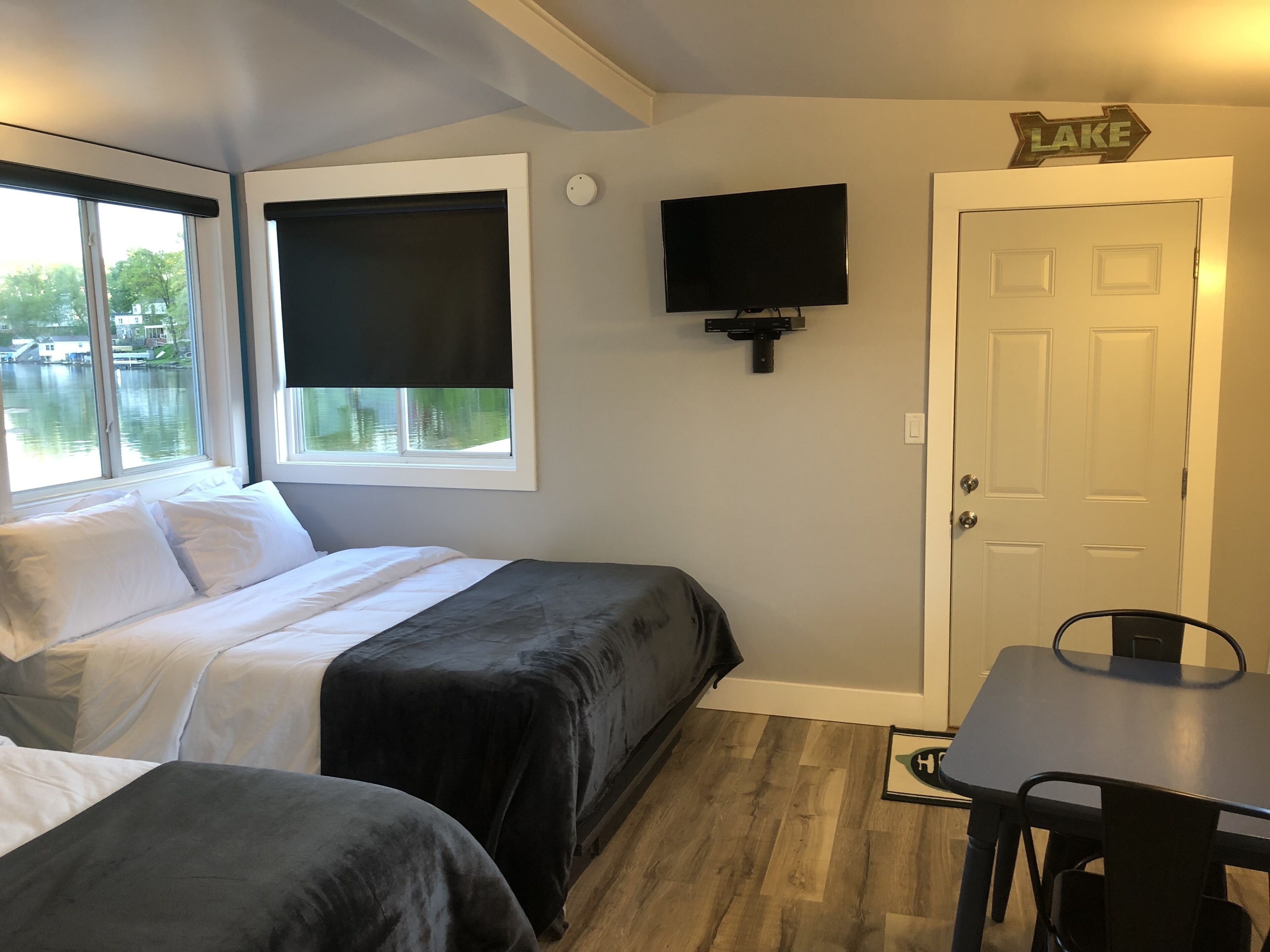 A room with two beds, a TV, a door, and a window overlooking a body of water.