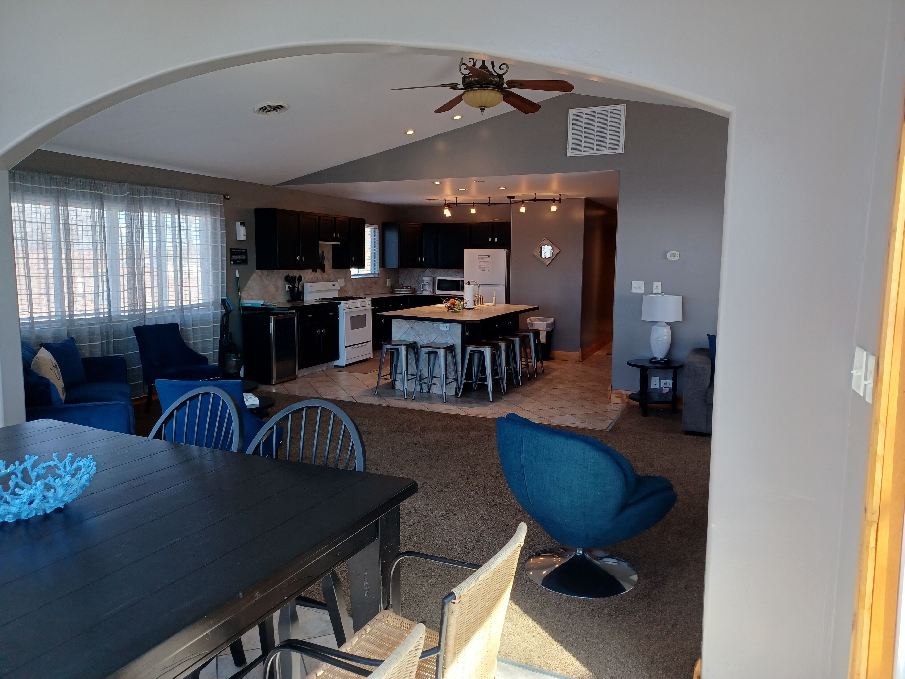 Uma sala de estar espaçosa com uma mesa de jantar de madeira escura, cadeiras azuis e uma área de cozinha com ilha central.
