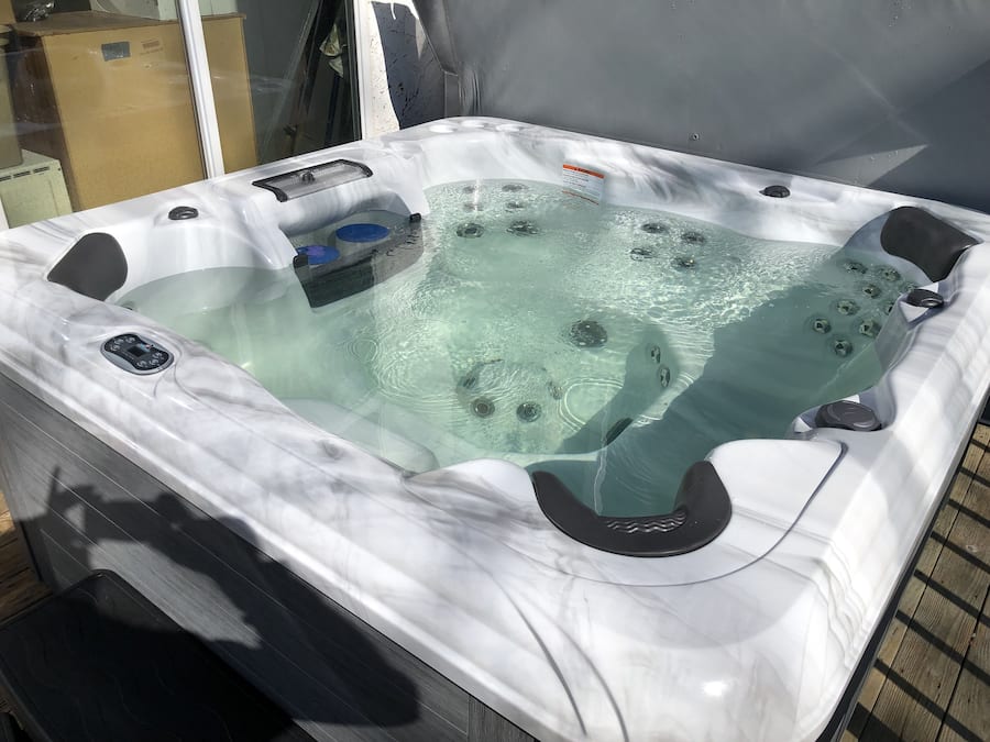 A hot tub with a control panel, a glass top, and a wooden deck surrounding it.