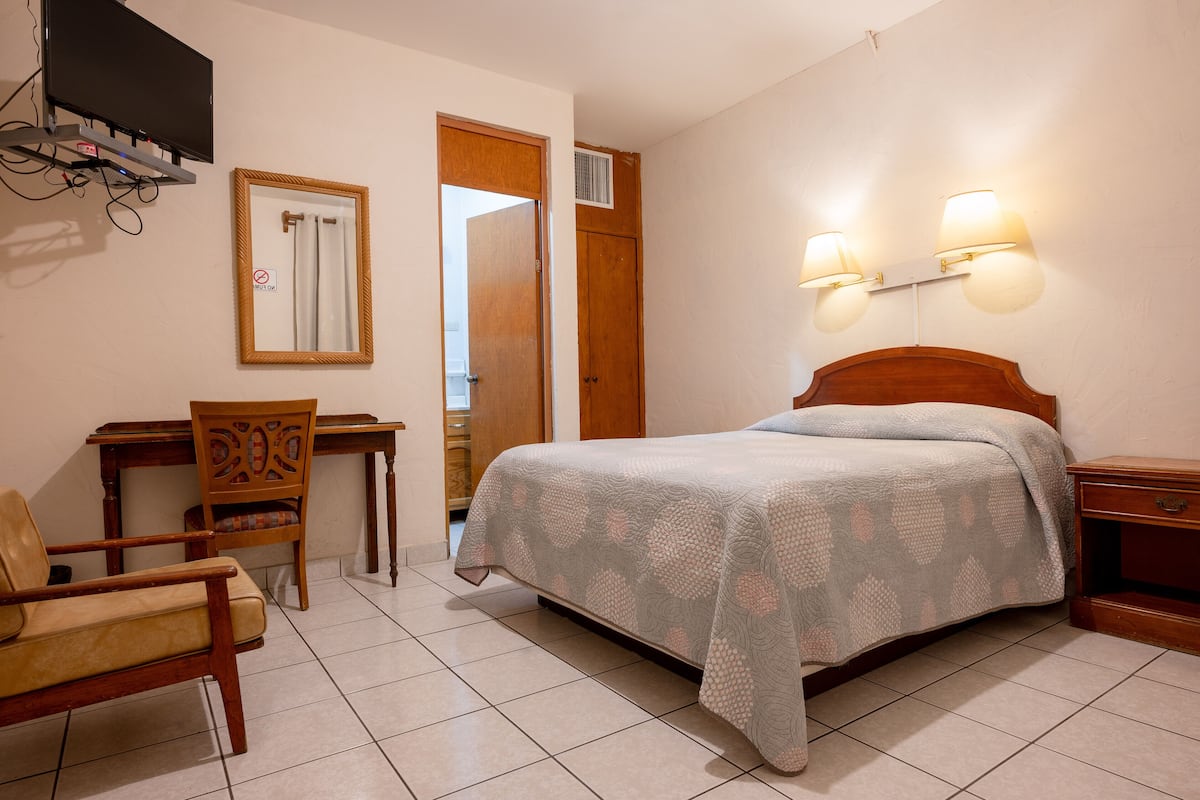 Ein Schlafzimmer mit einem Bett, einem Schreibtisch, einem Sessel und einem an der Wand montierten Fernseher.