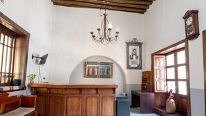 Een kamer met een houten receptiebalie, een kroonluchter, een klok en een groot raam.