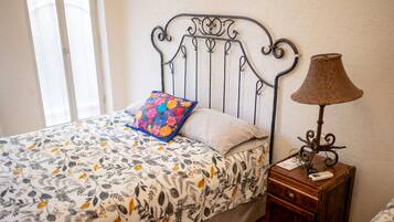 A bed with a patterned bedspread, a decorative pillow, a bedside lamp, and a small wooden nightstand.