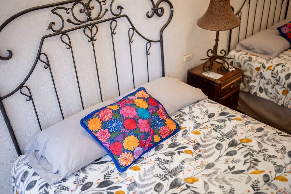 Ein Bett mit einem blumigen Überwurf und einem farbenfrohen, gesteckten Kissen.