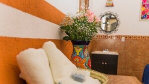 Een badkamer met een gevlochten mand vol witte handdoeken, een kleurrijke vaas met bloemen, en een spiegel aan de muur.