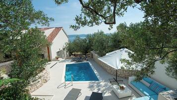 A pool area with a rectangular pool, lounge chairs, a white umbrella, and a stone wall.