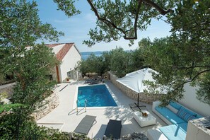 A pool area with a rectangular pool, lounge chairs, a white umbrella, and a stone wall. - Villa Olive Tree (Omis)