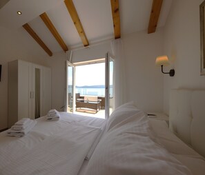 A bedroom with a large bed, a view of the sea through an open door, a balcony with a table and chairs, and a wardrobe. - Villa Olive Tree (Omis)